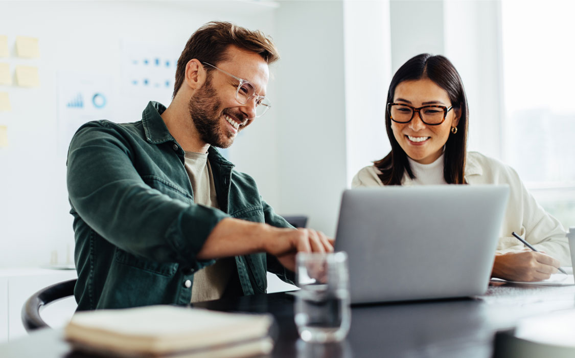 Two colleagues are happily collaborating and sharing a moment of laughter during a meeting in a bright office.