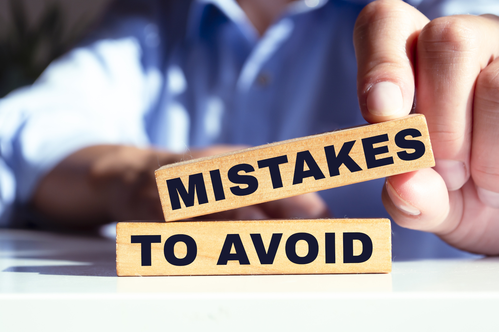 The image shows a person holding two wooden blocks with the words "MISTAKES" and "TO AVOID," emphasizing the importance of avoiding mistakes.