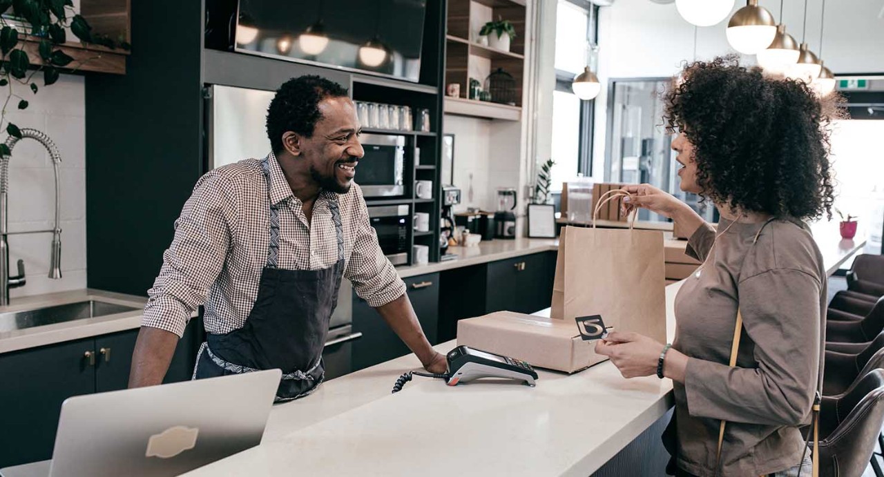 A woman is paying for her purchase at a café counter while the barista happily attends to her.