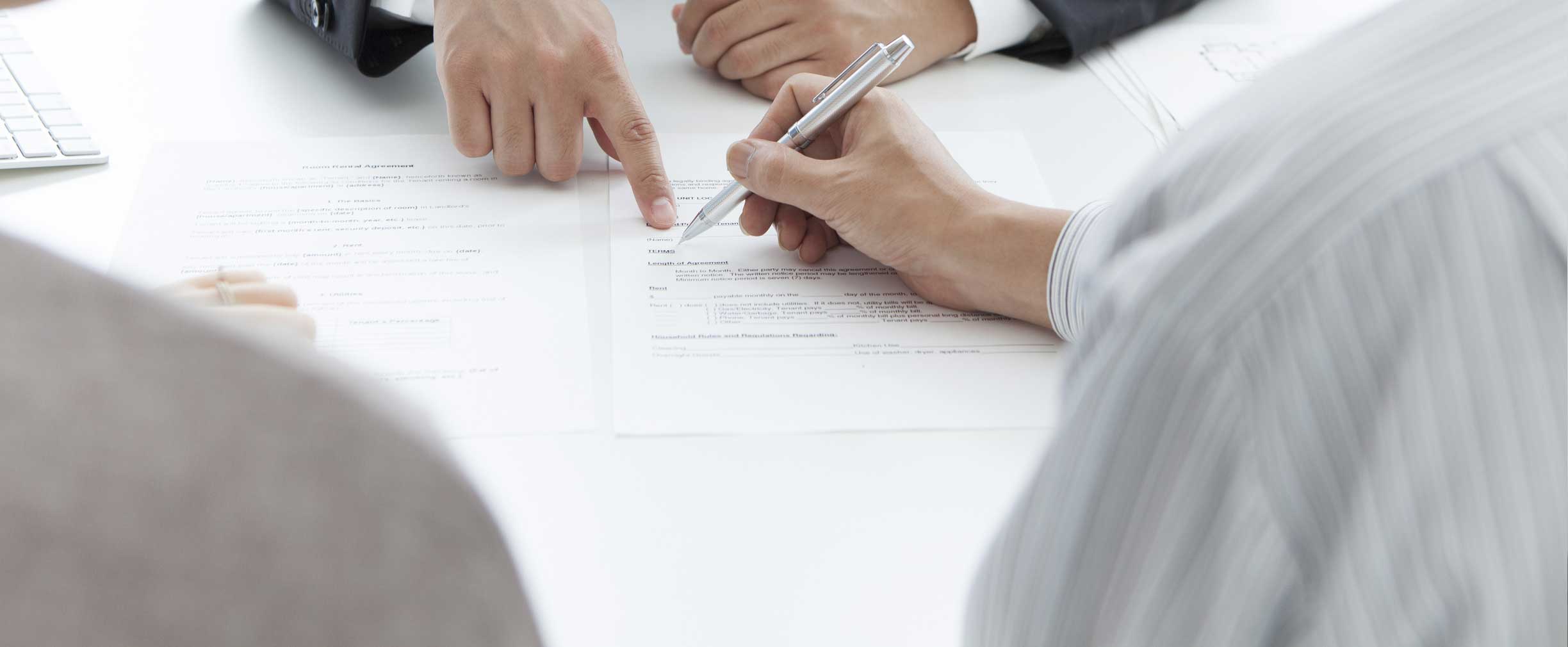Two individuals are signing and pointing to documents, likely engaged in a formal agreement or contract discussion.