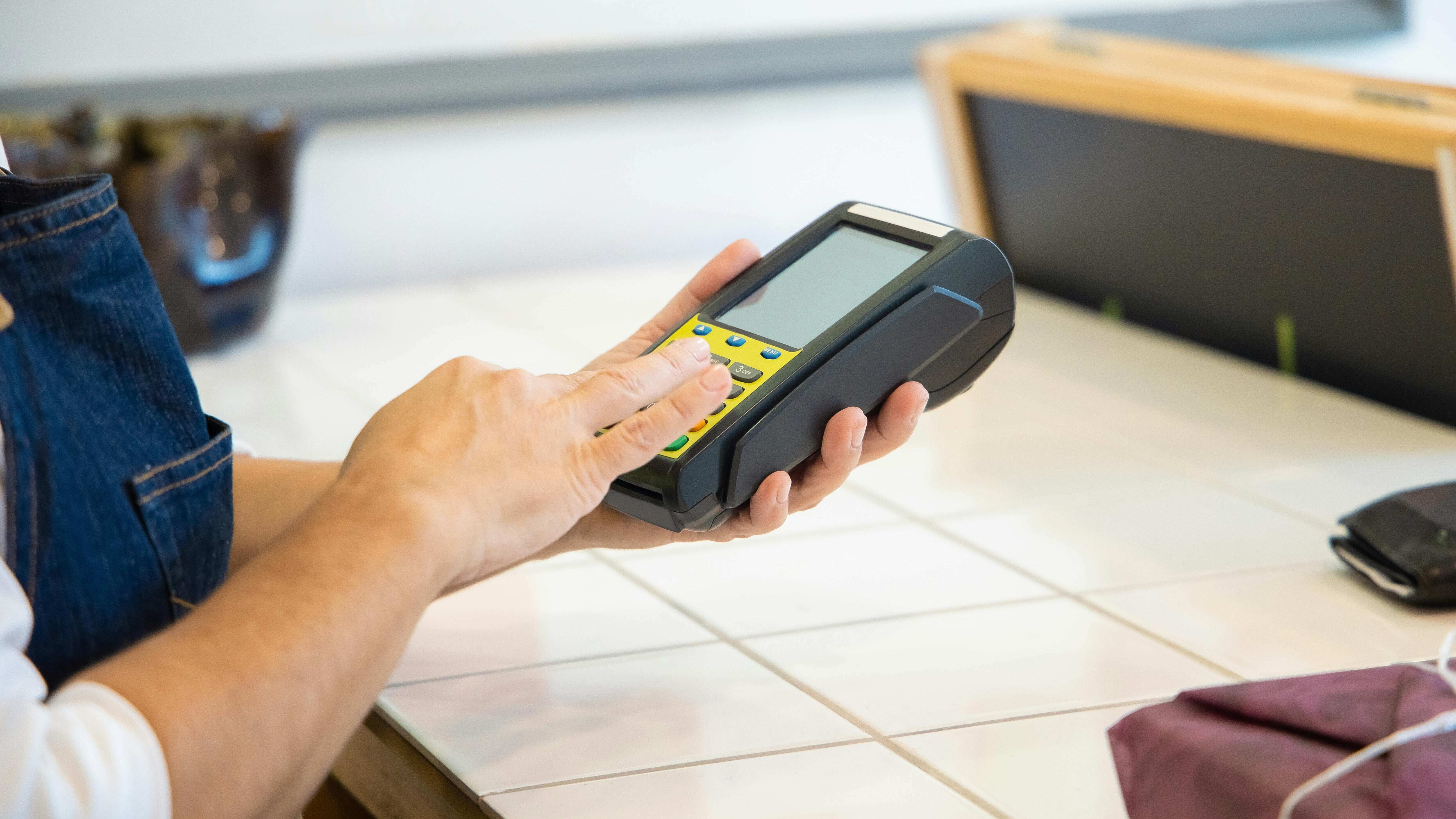 A person using a handheld electronic payment terminal on a tiled countertop.