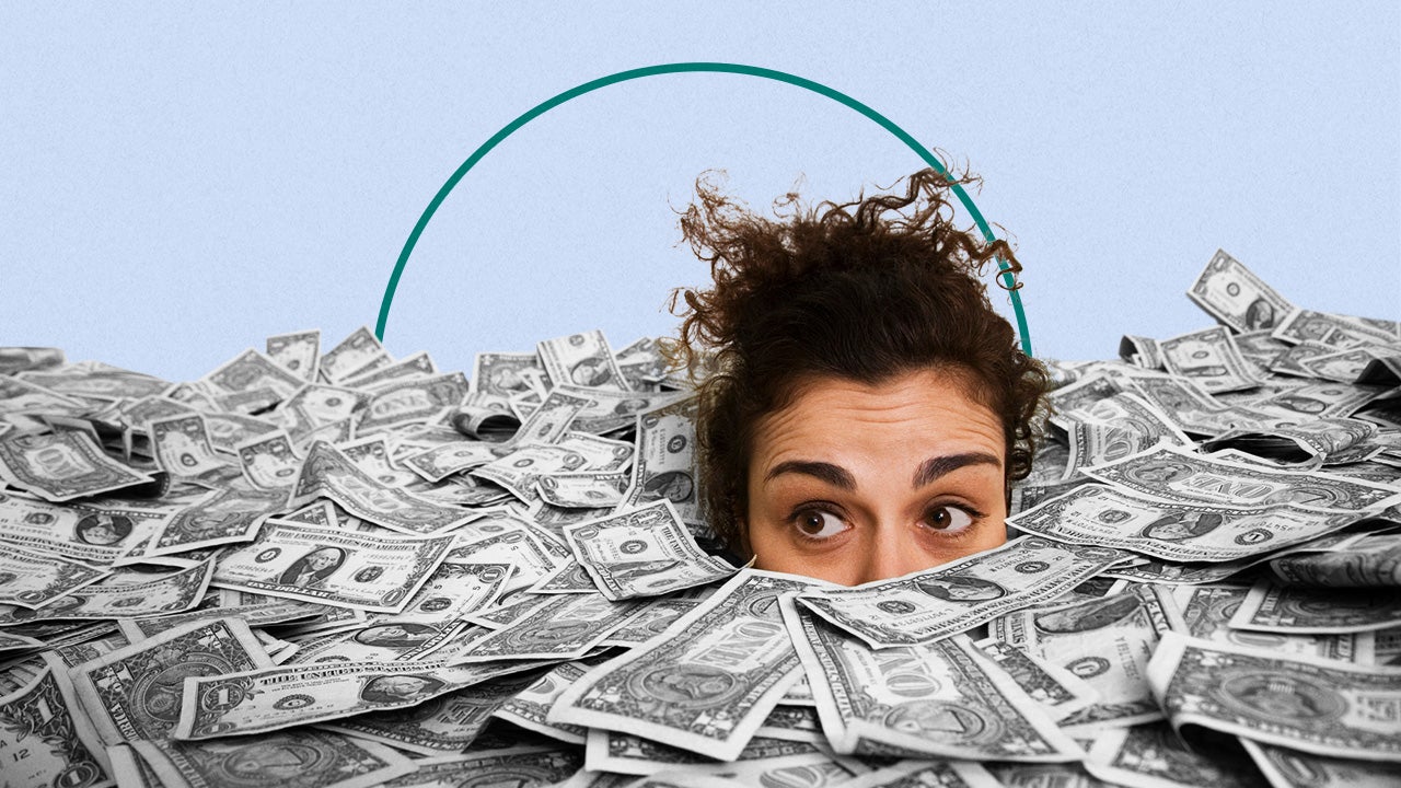 A woman peeking out from a large pile of scattered US dollar bills, appearing curious or overwhelmed.