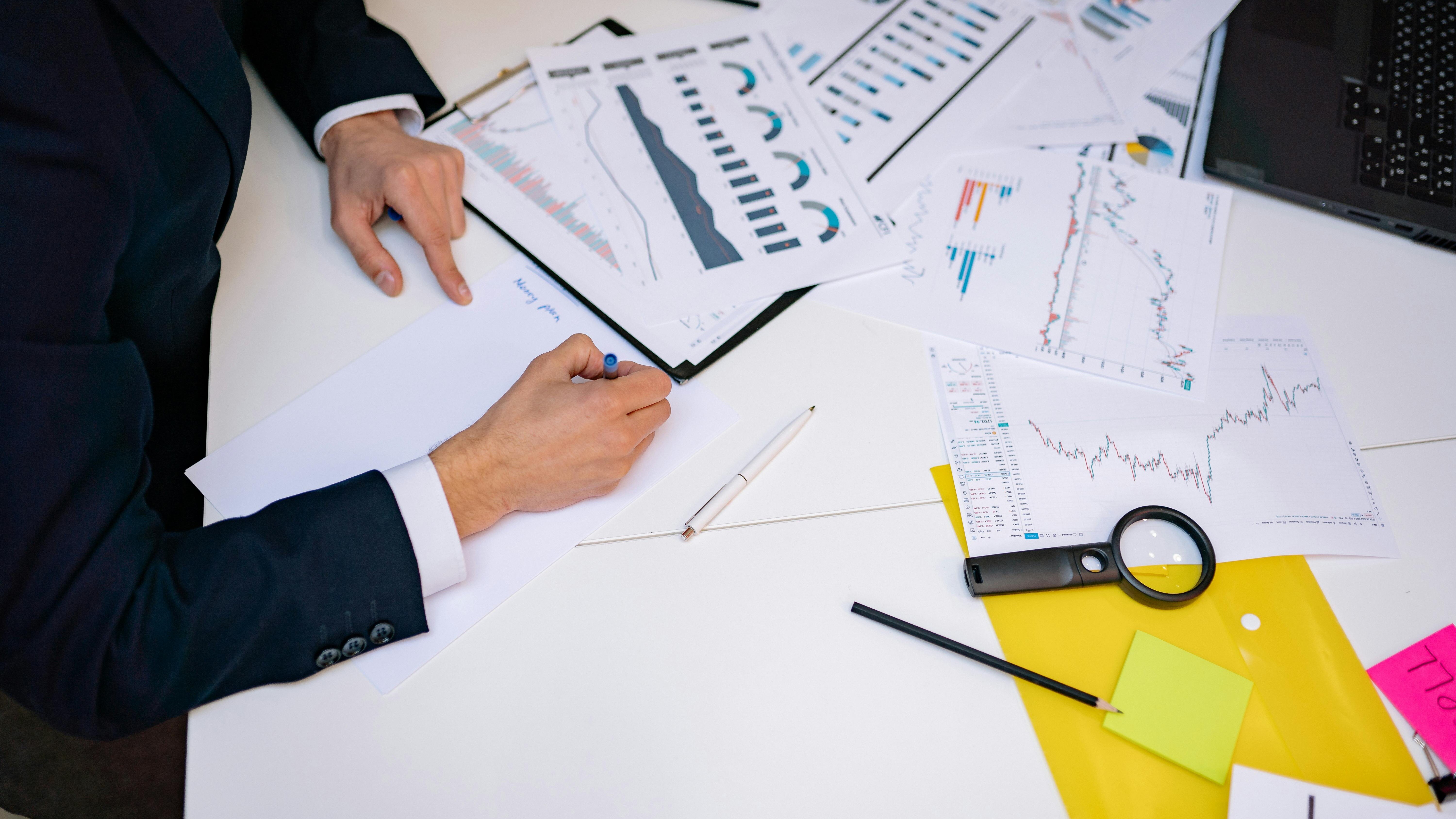 A person working at a desk surrounded by financial charts, graphs, and documents, analyzing data for business or investment purposes.