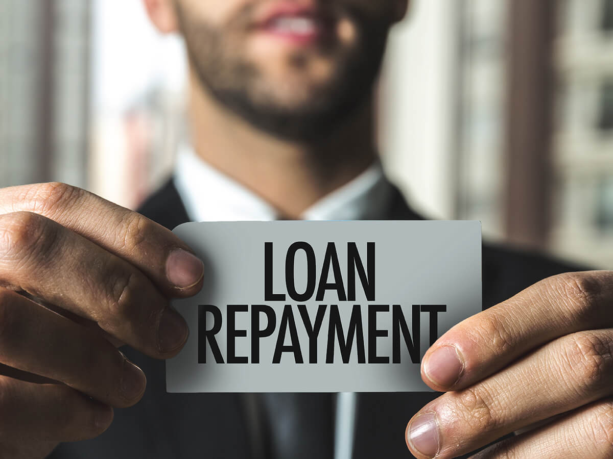 A man in a suit is holding a sign that says "LOAN REPAYMENT," indicating a focus on repaying borrowed money.