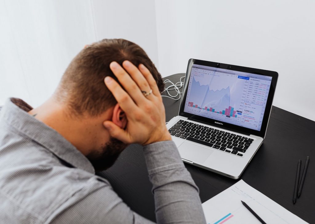 A man appears stressed or worried while analyzing declining financial data on his laptop screen.