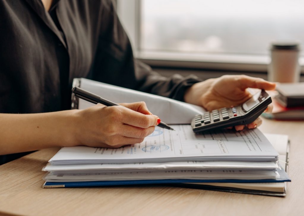 A person is reviewing financial documents, using a calculator and pen, possibly analyzing finances or preparing for accounting tasks.