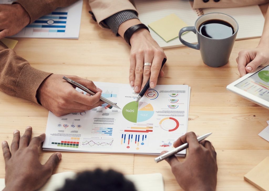 The image shows a group of people analyzing financial data and charts during a meeting or discussion.