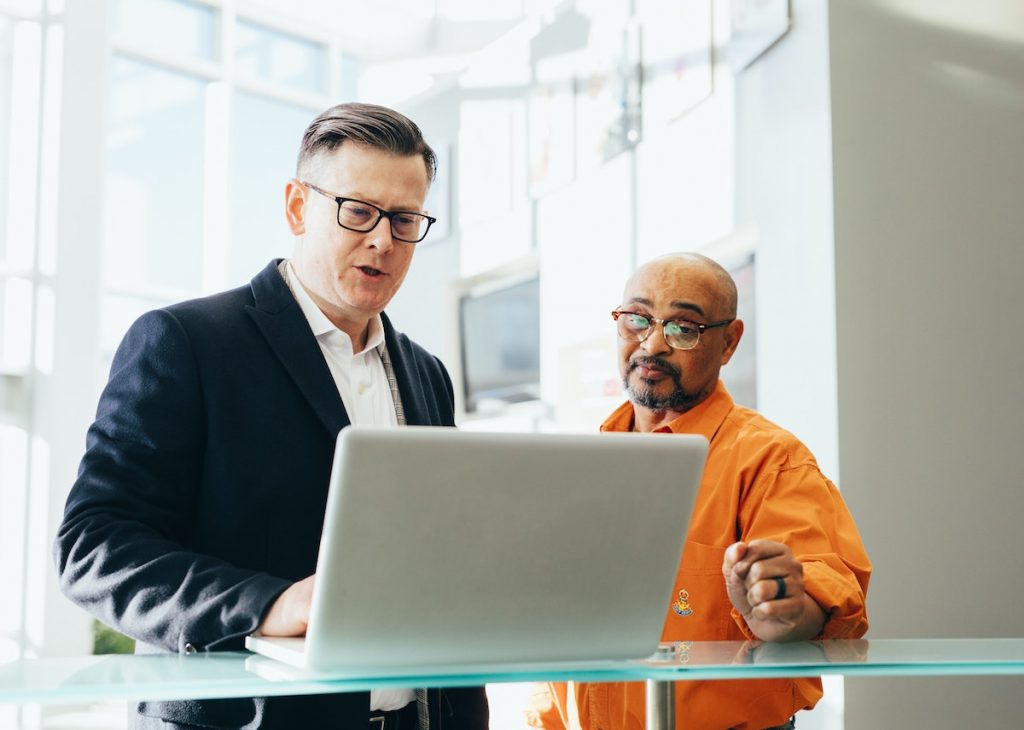 Two men are having a serious discussion while looking at a laptop in a bright, modern indoor setting.