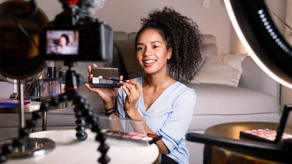 A woman is recording a makeup tutorial or review in a well-lit indoor setting.