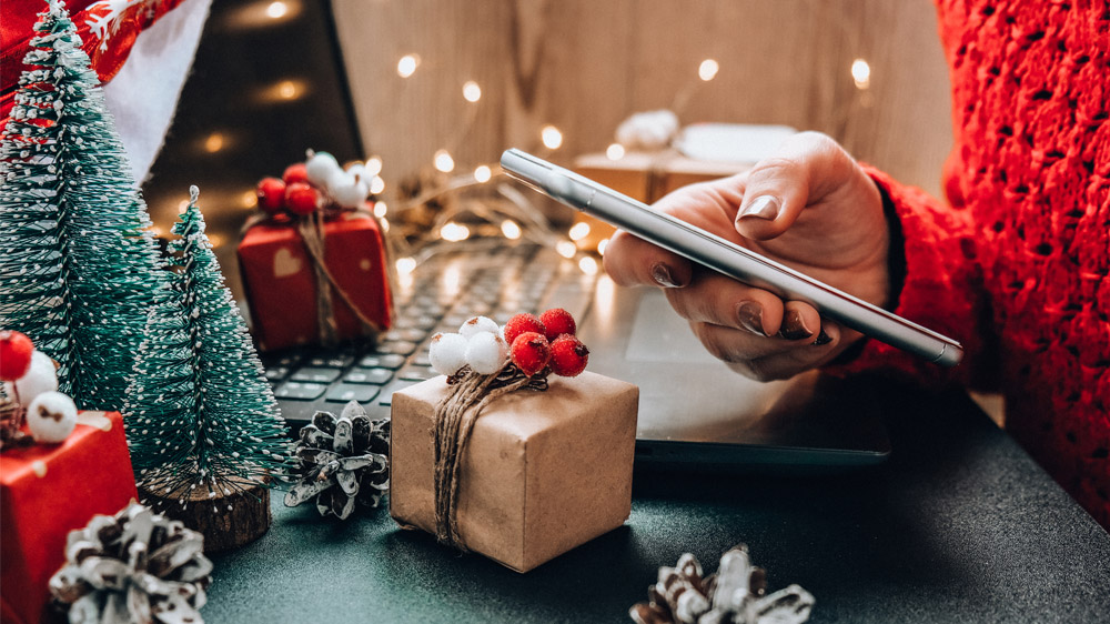 A person in a red sweater is using a smartphone amidst Christmas decorations and small wrapped presents.