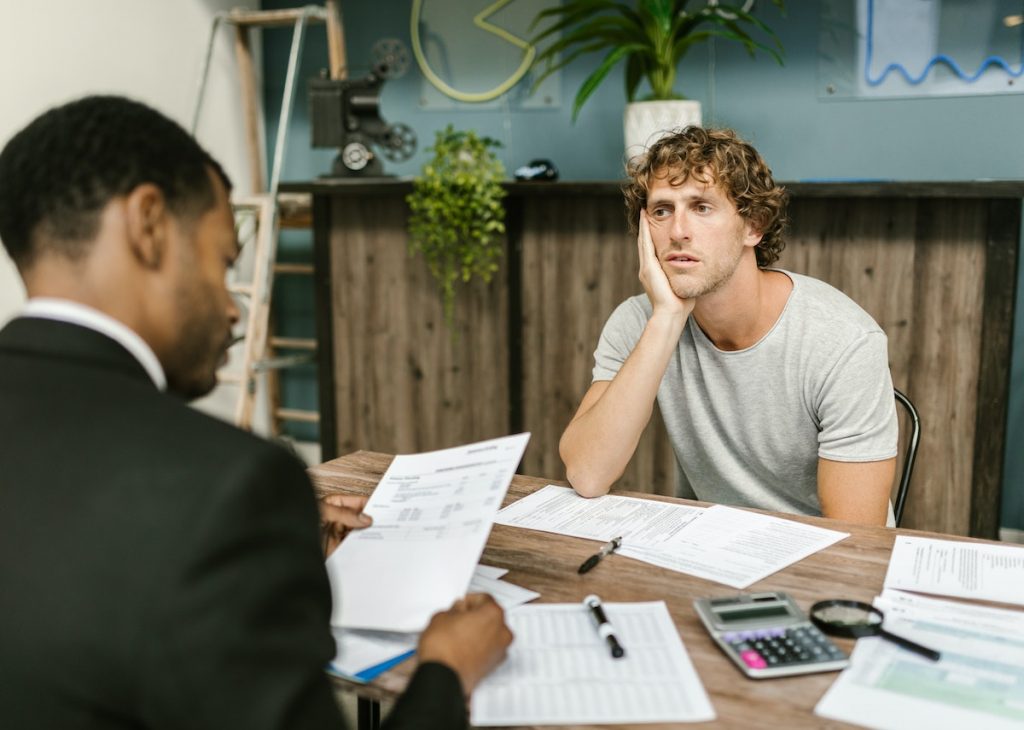 A man appears worried or stressed while discussing documents with a professional across the table.