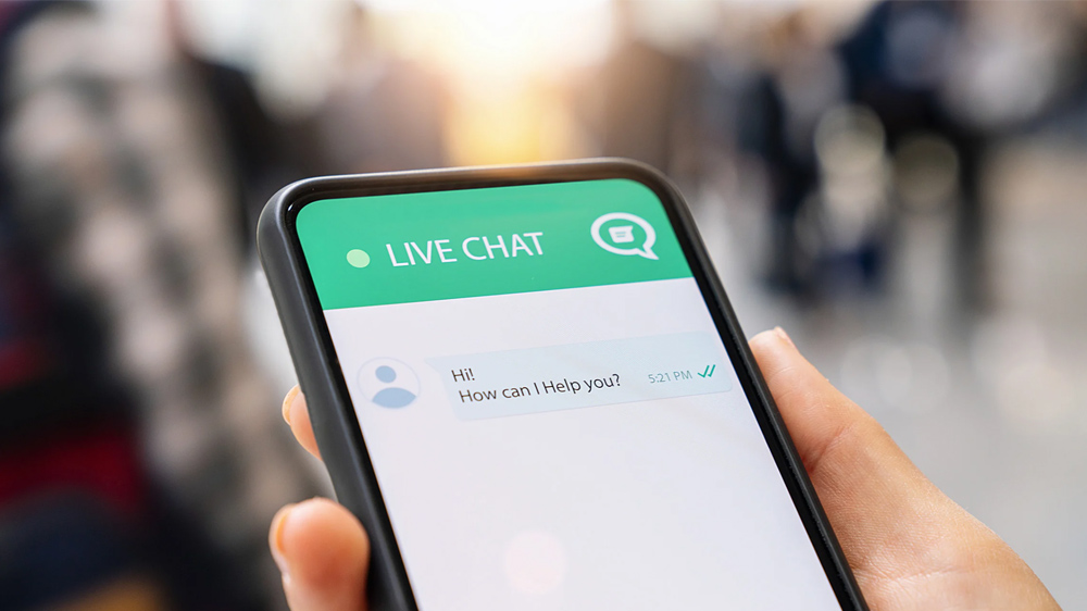 The image shows a person holding a smartphone with a live chat support conversation on the screen.