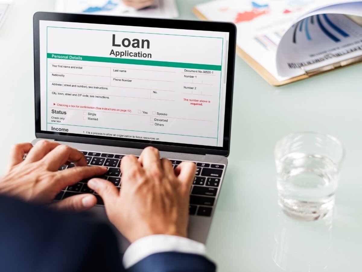 The image shows a person filling out a loan application form on a laptop.