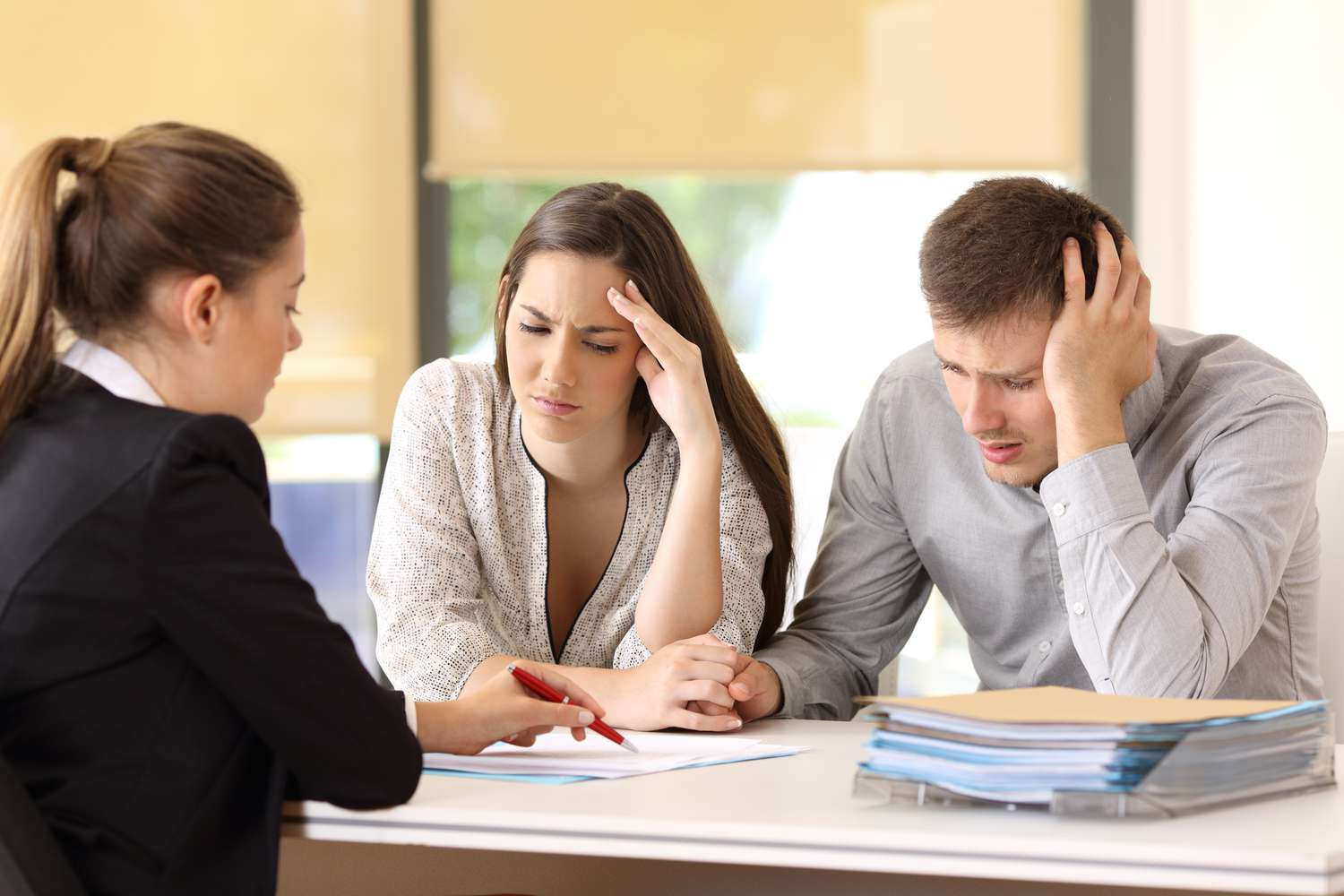 The image depicts a couple looking distressed and worried while discussing their financial problems with a financial advisor.