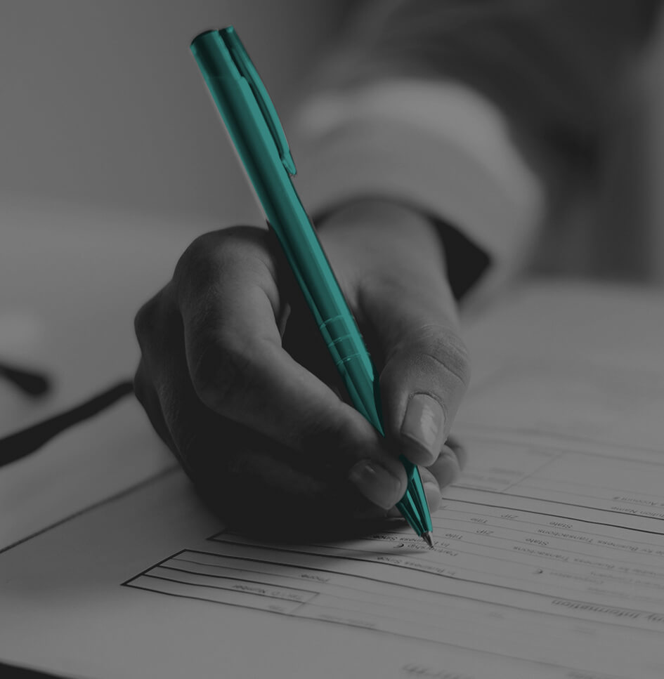 The image shows a person filling out a form or document with a pen.