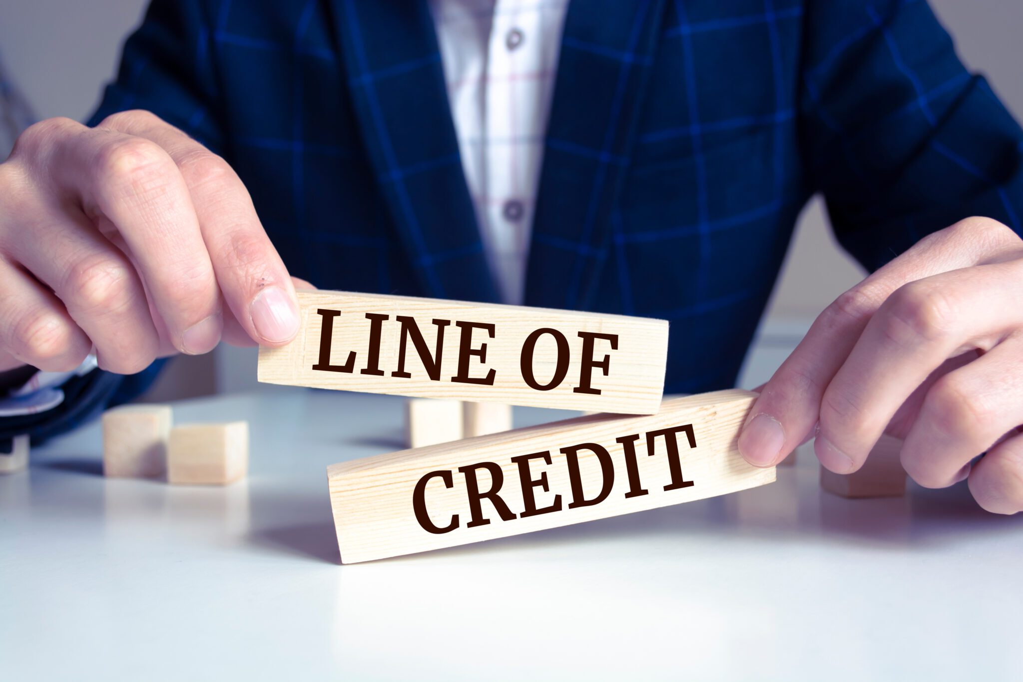 The image shows a person arranging wooden blocks with the words "LINE OF CREDIT" to illustrate the concept of a flexible borrowing limit.
