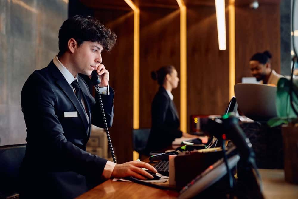 A hotel receptionist is handling a phone call while working at the front desk.