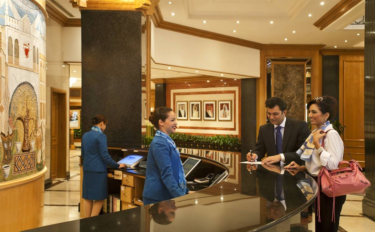 The image shows a hotel reception area where a guest is checking in with the help of staff behind the counter.