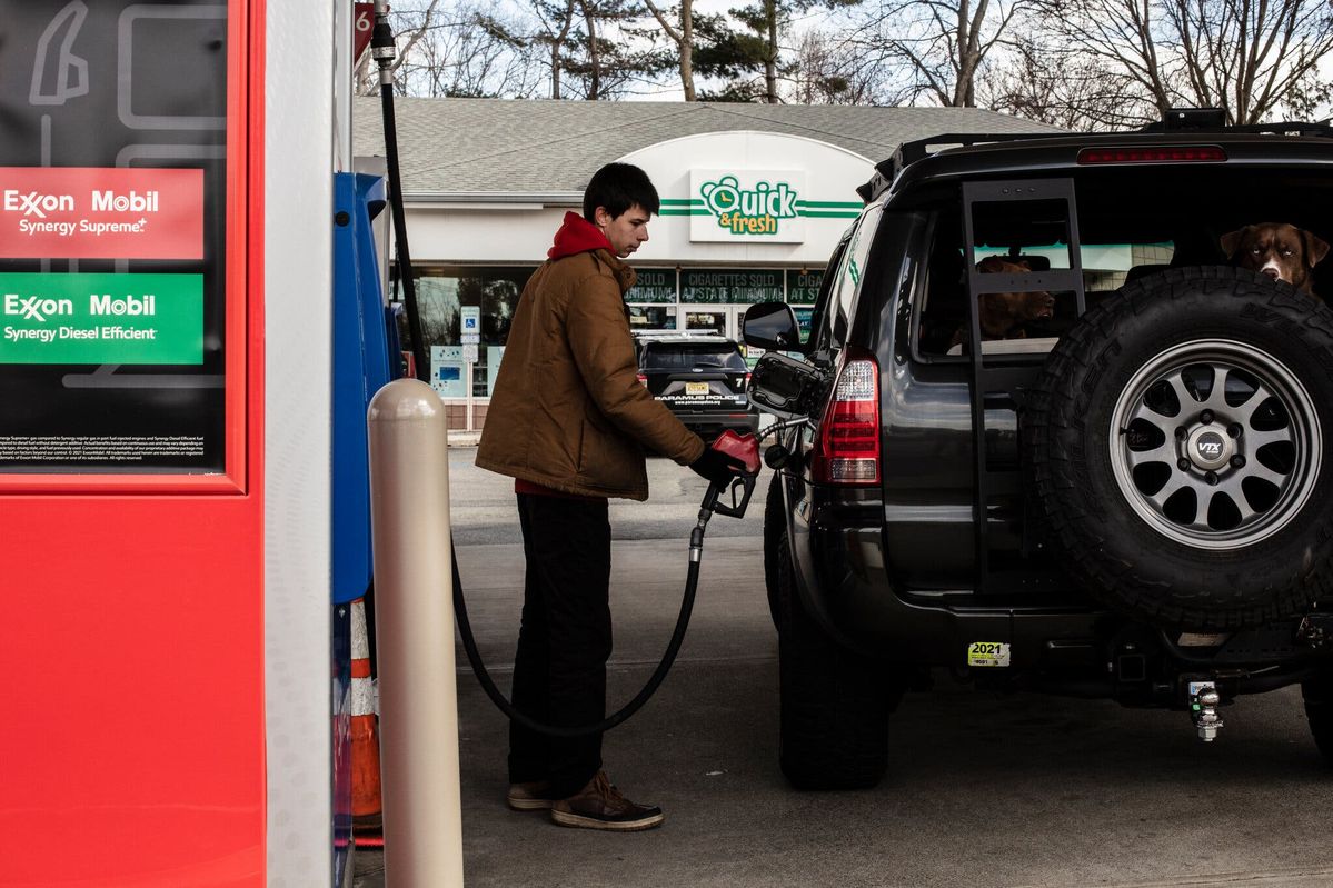 A person refueling a black SUV at a gas station with a dog inside the vehicle.