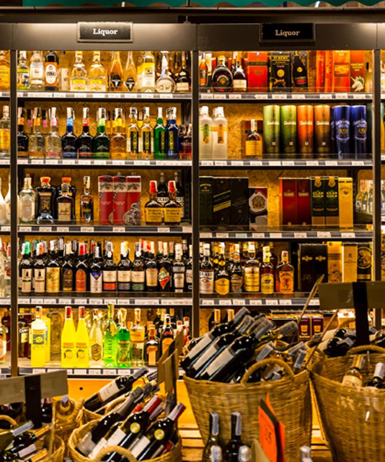 A liquor store display with shelves stocked with a variety of alcoholic beverages and bottles arranged in baskets at the front.