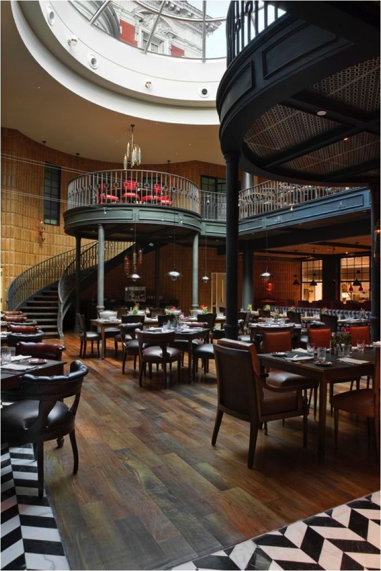 Elegant restaurant interior with a mezzanine level, wooden accents, and both modern and classic furniture under natural light.