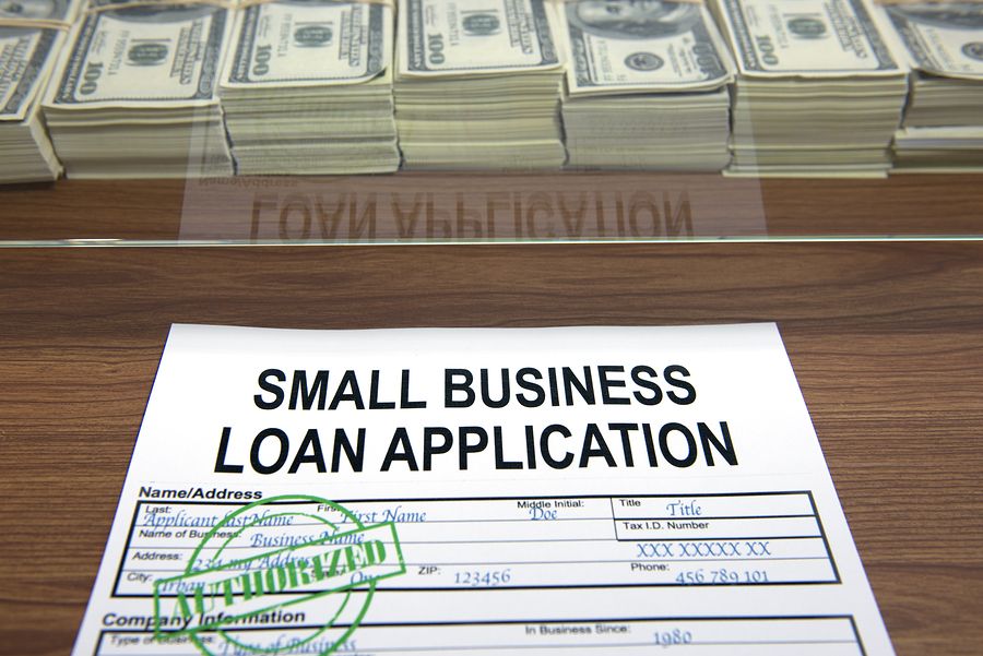 A small business loan application form with a green "APPROVED" stamp placed on top, positioned on a wooden desk.
