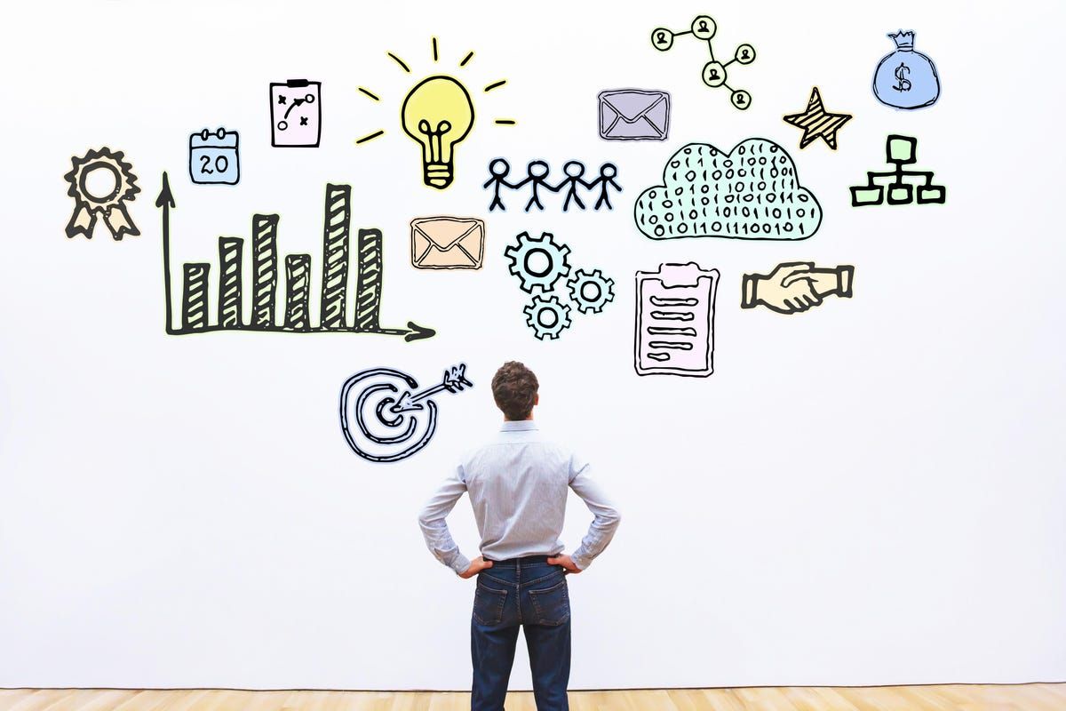 A businessman stands facing a white wall filled with hand-drawn icons representing business growth, strategy, innovation, teamwork, and financial planning.