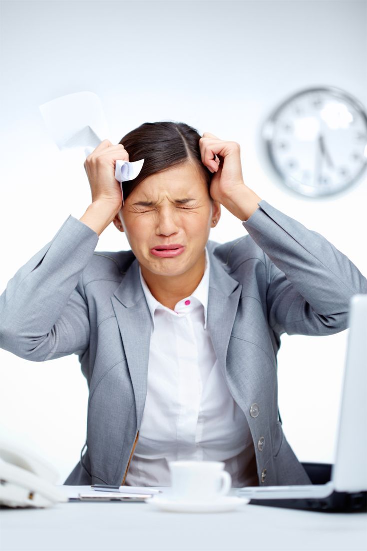 A stressed businesswoman sitting at a desk, holding papers to her head with eyes closed, showing frustration and pressure at work, with a clock in the background.