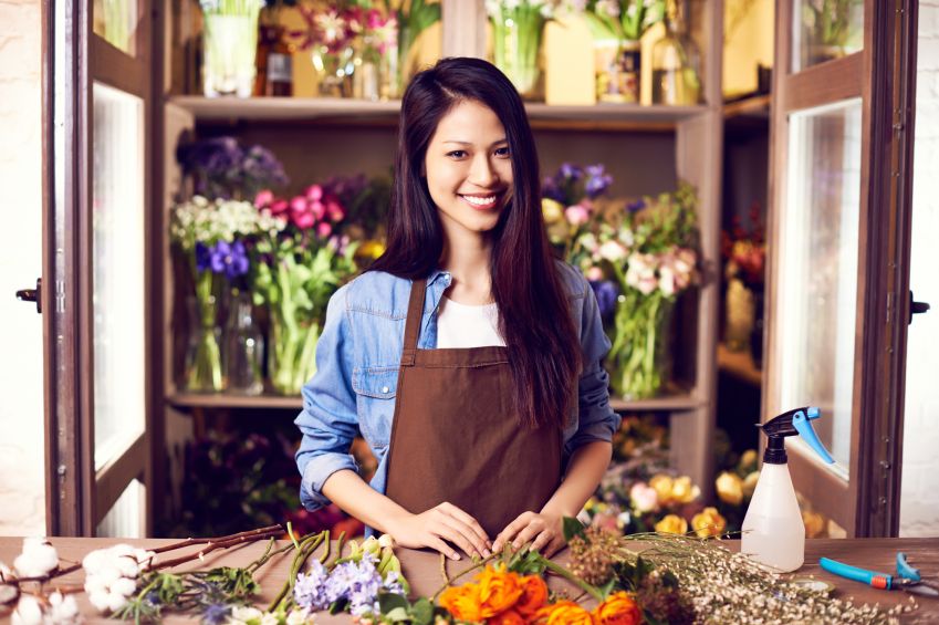 Smiling woman florist arranging fresh flowers in her shop, representing government-backed small business loans for women entrepreneurs to grow retail and creative businesses.