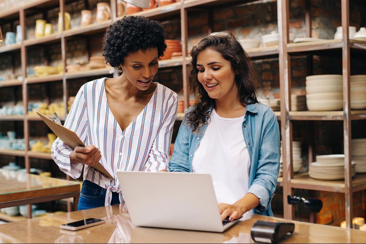 Two female small business owners reviewing finances on a laptop in their retail shop, representing small business loans for female entrepreneurs to support growth and daily operations.
