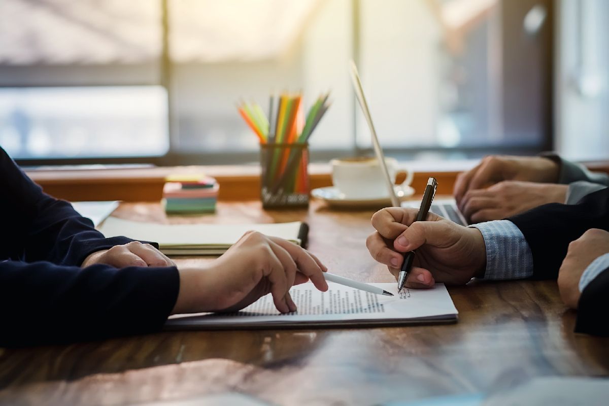 Nonprofit representatives signing loan documents at a desk with laptops and coffee, symbolizing business loans and funding support for nonprofit organizations.