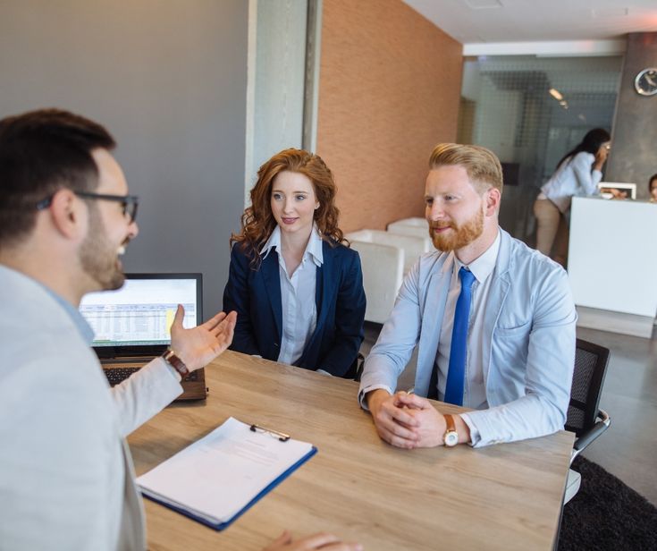 Business advisor talking with two clients at office desk discussing funding options paperwork and financial planning for small cleaning company.