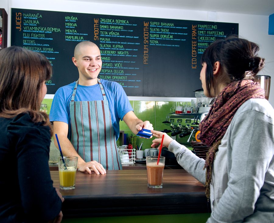 Small business owner accepting a credit card payment from a customer at a café counter, representing merchant cash advance funding solutions that help small businesses manage cash flow and grow.
