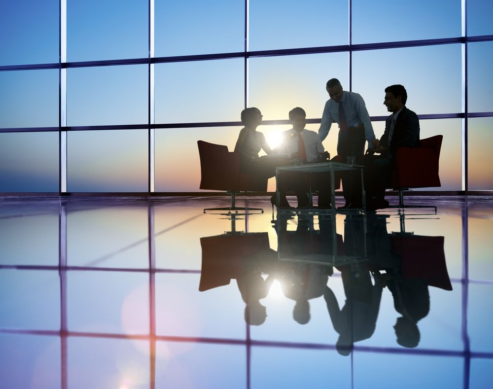 Silhouetted business professionals meeting in a modern office with large windows at sunset, symbolizing collaboration and funding solutions like merchant cash advance in Washington.
